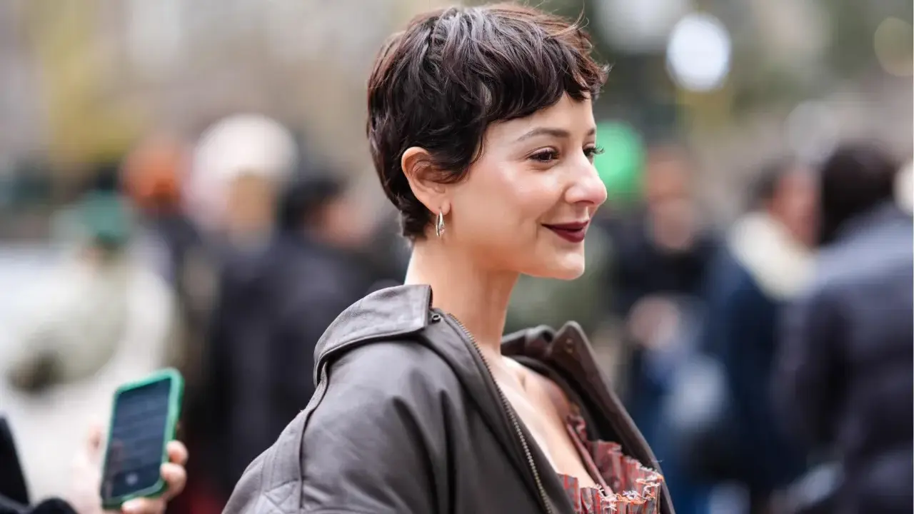 Frau mit einem langen Pixie-Haarschnitt, dunklem Lederjacke und auffälligem Kleid.
