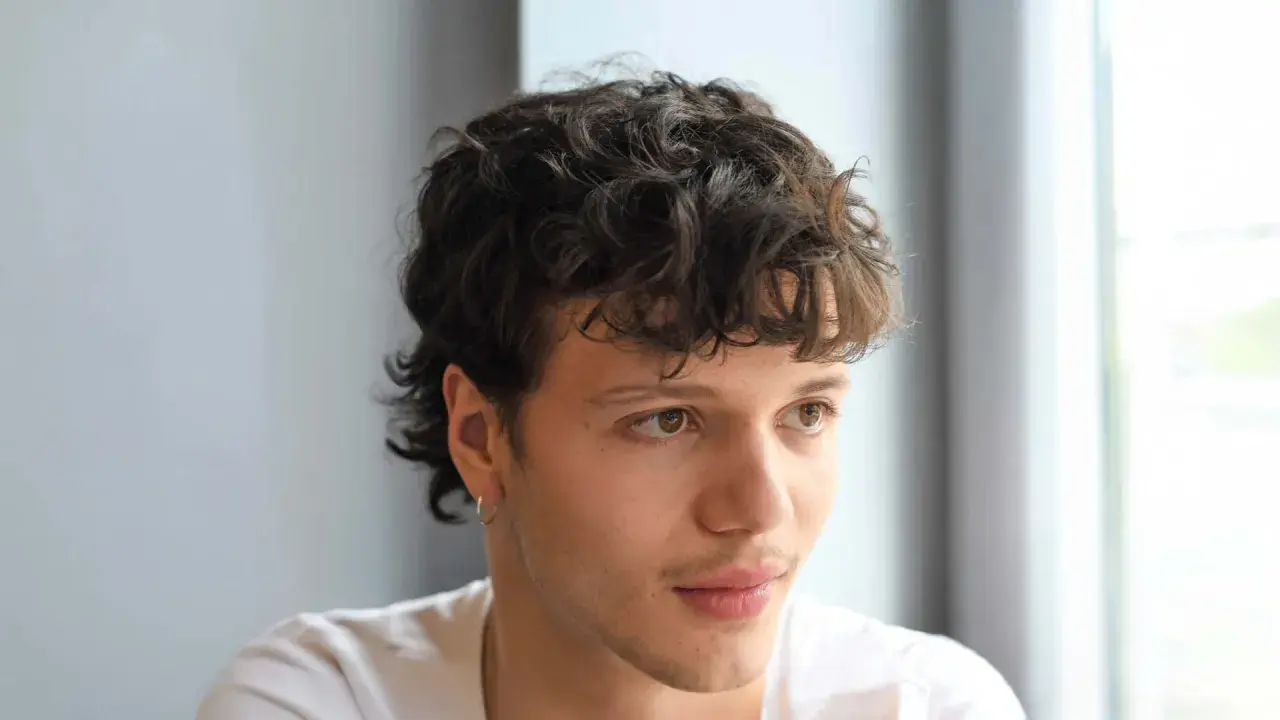 Junger Mann mit lockigem, kurzem Mullet-Haarschnitt und einem dezenten Ringohrring.