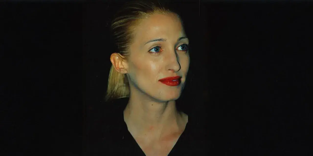 Frau mit blondem Pferdeschwanz und rotem Lippenstift, im **Carolyn Bessette-Kennedy Style**, blickt nach rechts.