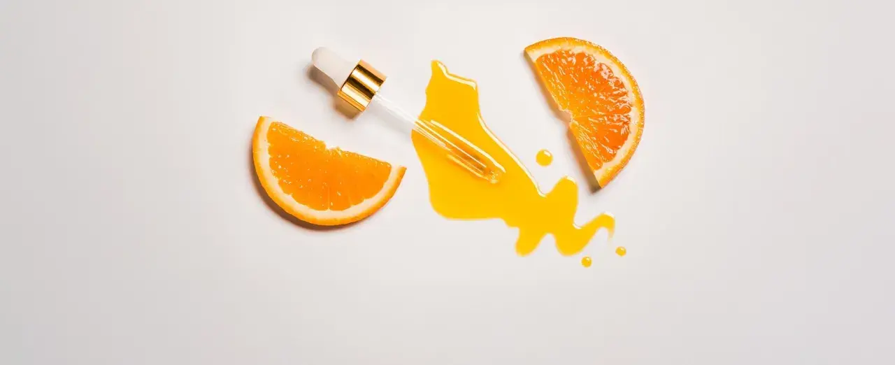 Ein Pipettenfläschchen mit leuchtend gelbem Vitamin C Serum, umgeben von saftigen Orangenscheiben. Morgens oder abends für strahlende Haut.