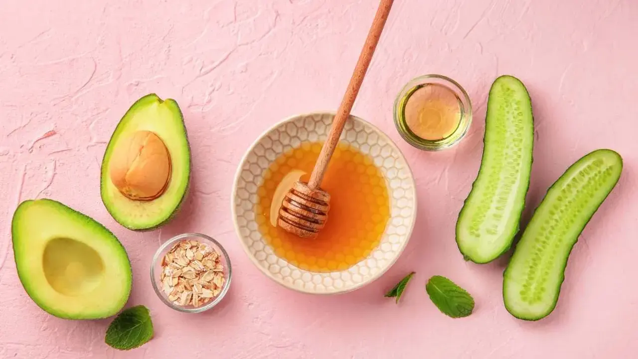 Zutaten für eine Gesichtsmaske selber machen: Avocado, Honig, Haferflocken, Gurke und Öl auf rosa Untergrund.