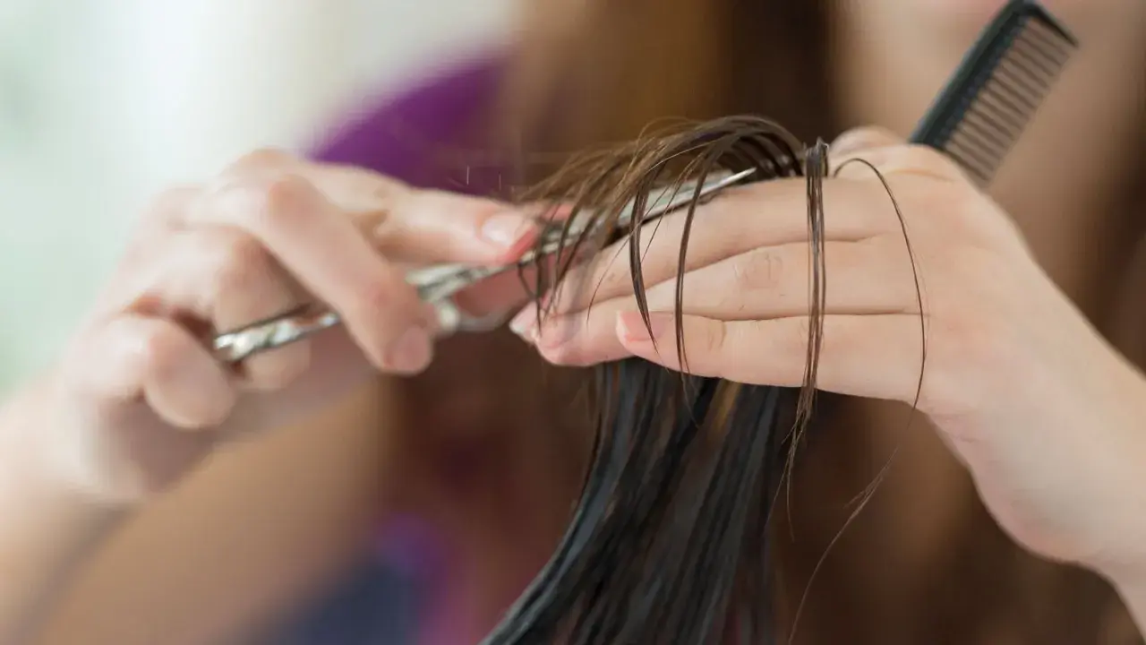 Hände schneiden feuchtes Haar mit einer Schere. Ein Kamm liegt bereit für den nächsten Schritt des jellyfish cut.