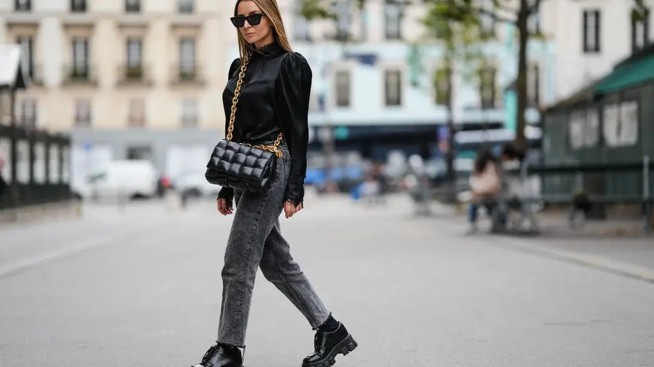 Stilvolle Frau in grauer Jeans, schwarzer Bluse und Plateau-Schuhen. Perfekt, um graue Jeans zu kombinieren!