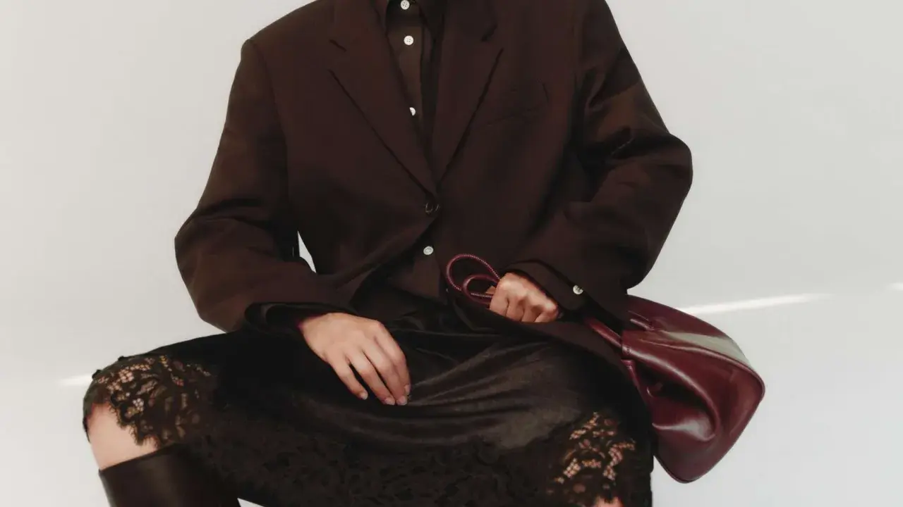 Elegant outfit: braun und schwarz kombinieren mit einem braunen Blazer, schwarzer Spitzenrock und Lederstiefel. Eine Hand hält eine weinrote Tasche.