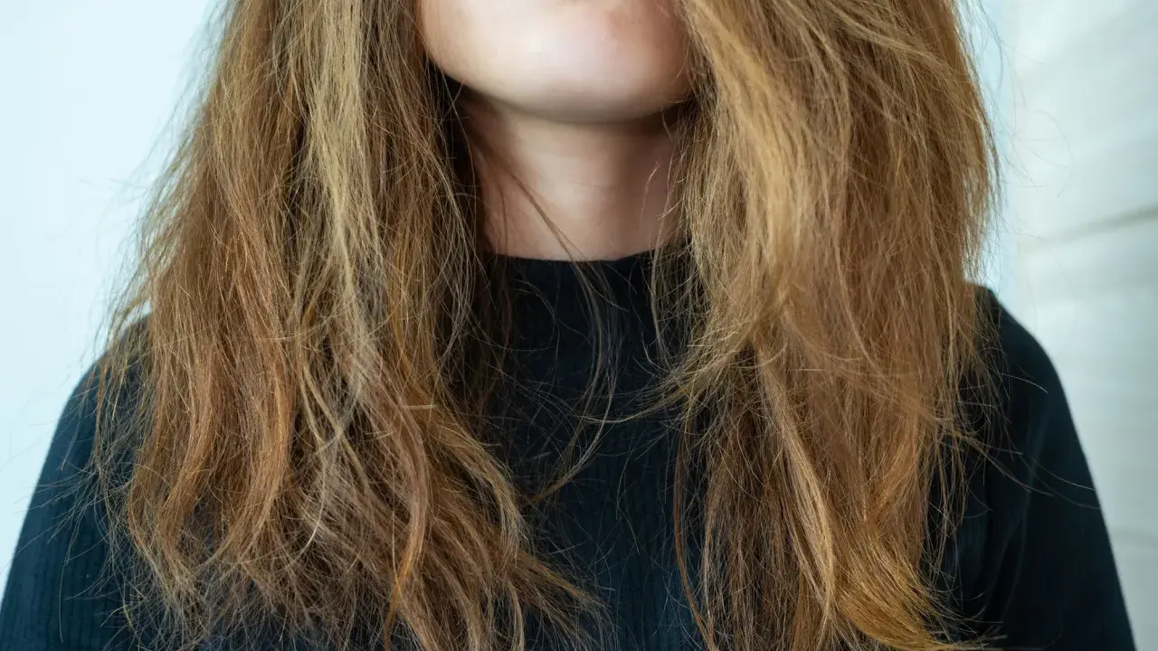 Frau mit zerzaustem, trockenem Haar, das ihr ins Gesicht fällt. Ihre Lippen sind leicht geöffnet und mit rosafarbenem Lippenstift bemalt.