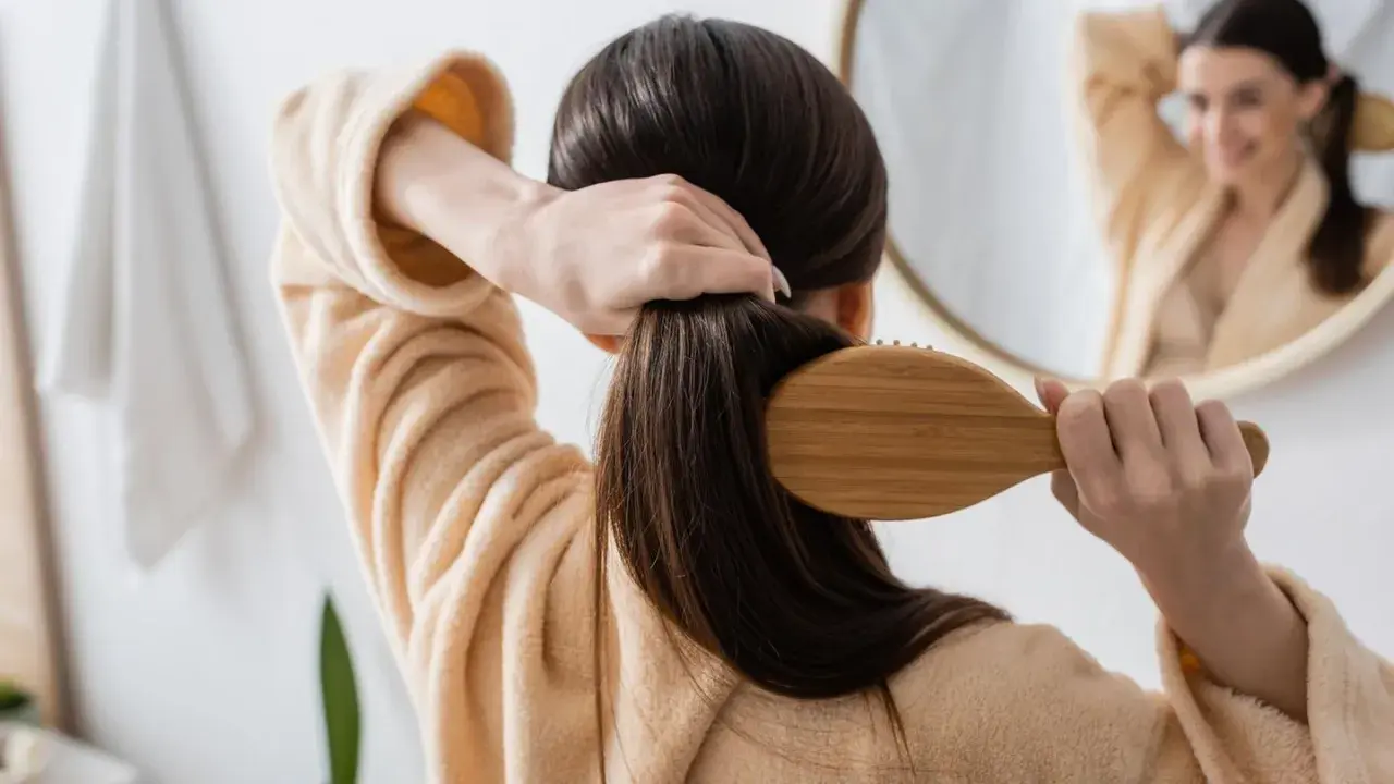 Frau kämmt ihr langes, dunkles Haar mit einer Holzbürste. Sie trägt einen flauschigen Bademantel. Tipps, wie wachsen haare schneller, sind hier nicht sichtbar.