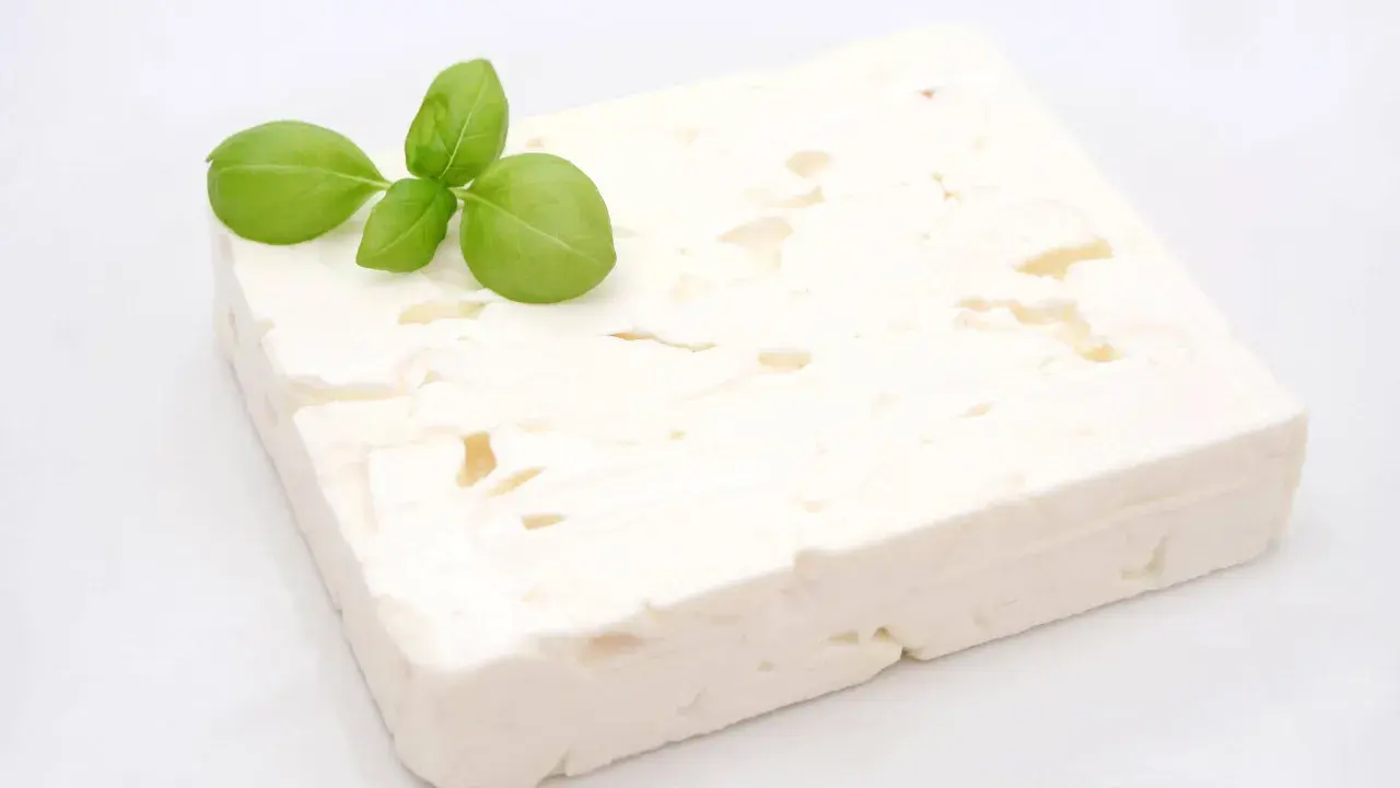 Ein Block Feta-Käse mit Basilikumblättern. Ist Feta gesund? Ja, er liefert Kalzium und Proteine.