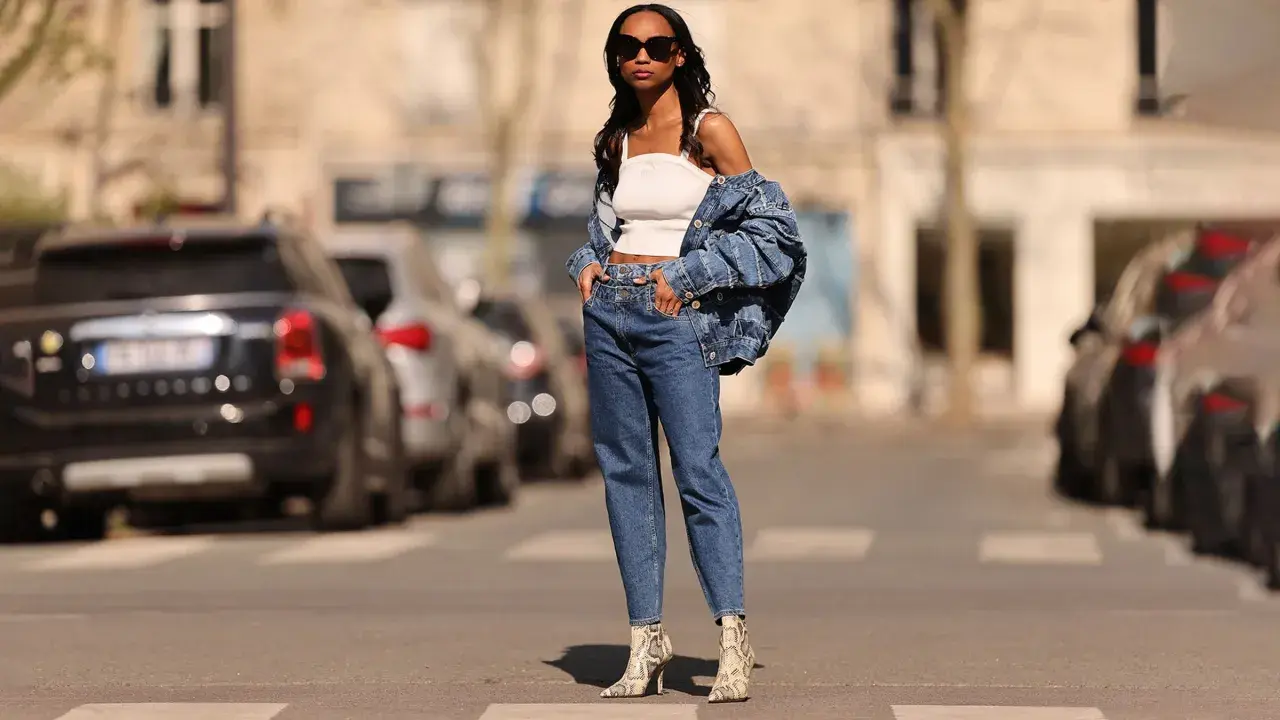 Stylisches Outfit: Eine Frau kombiniert barrel jeans mit einem weißen Top und Jeansjacke. Schlangenleder-Stiefel runden den Look ab.