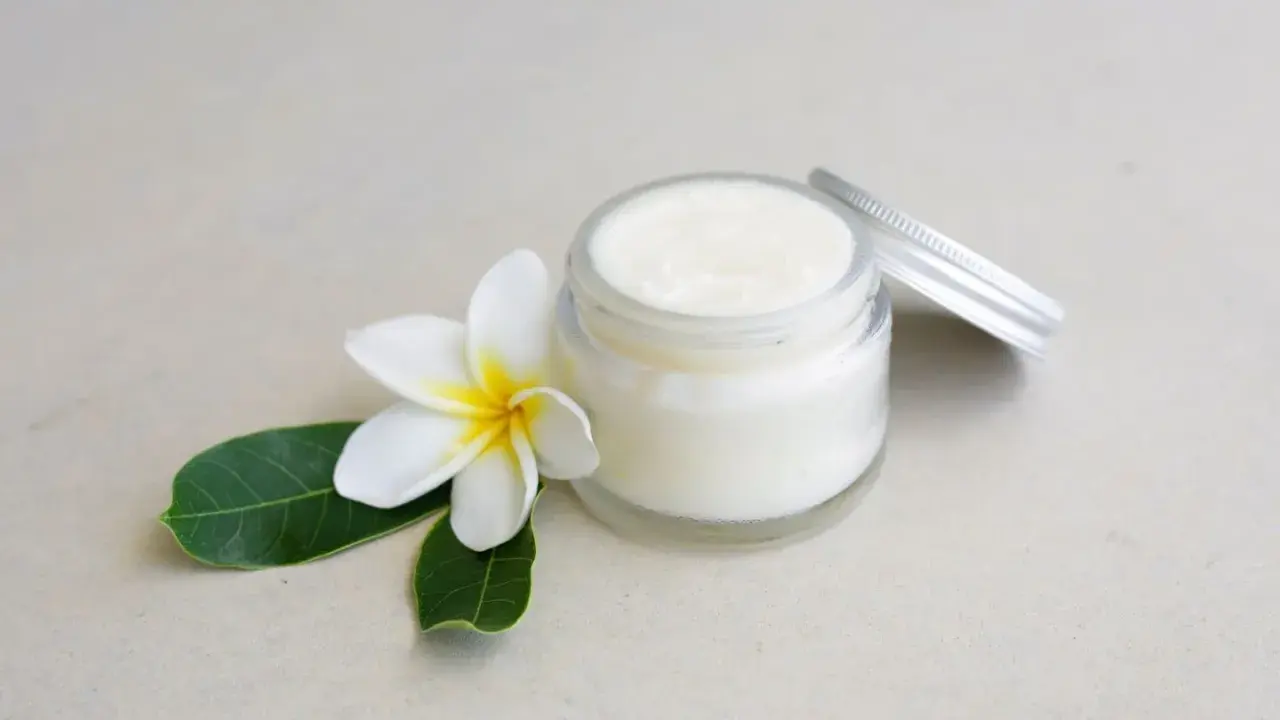Creme in einem Glas mit einer Blüte und Blättern. Perfekt, um Deo selber machen mit Sheabutter.
