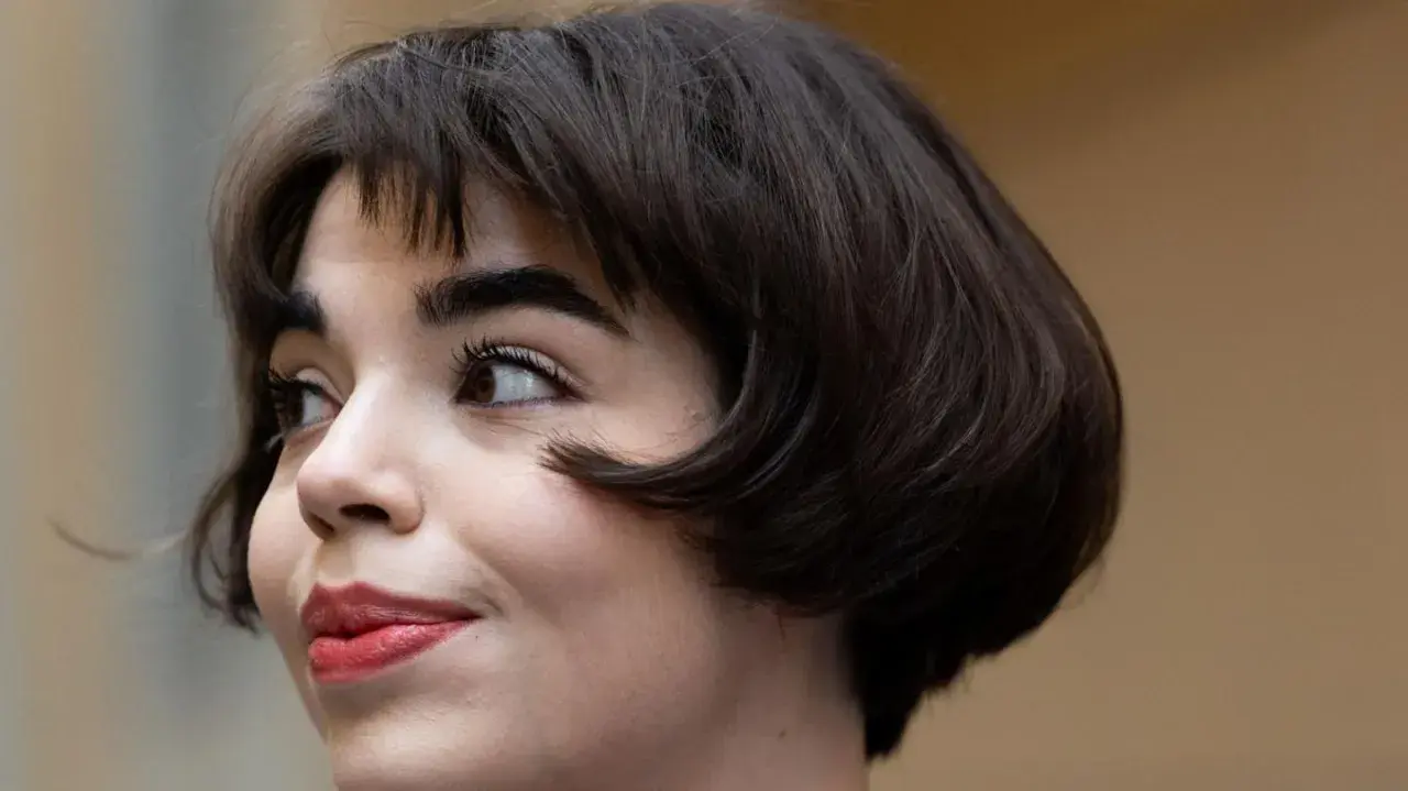Eine Frau mit einem eleganten, dunklen short bob und rotem Lippenstift blickt nach links.