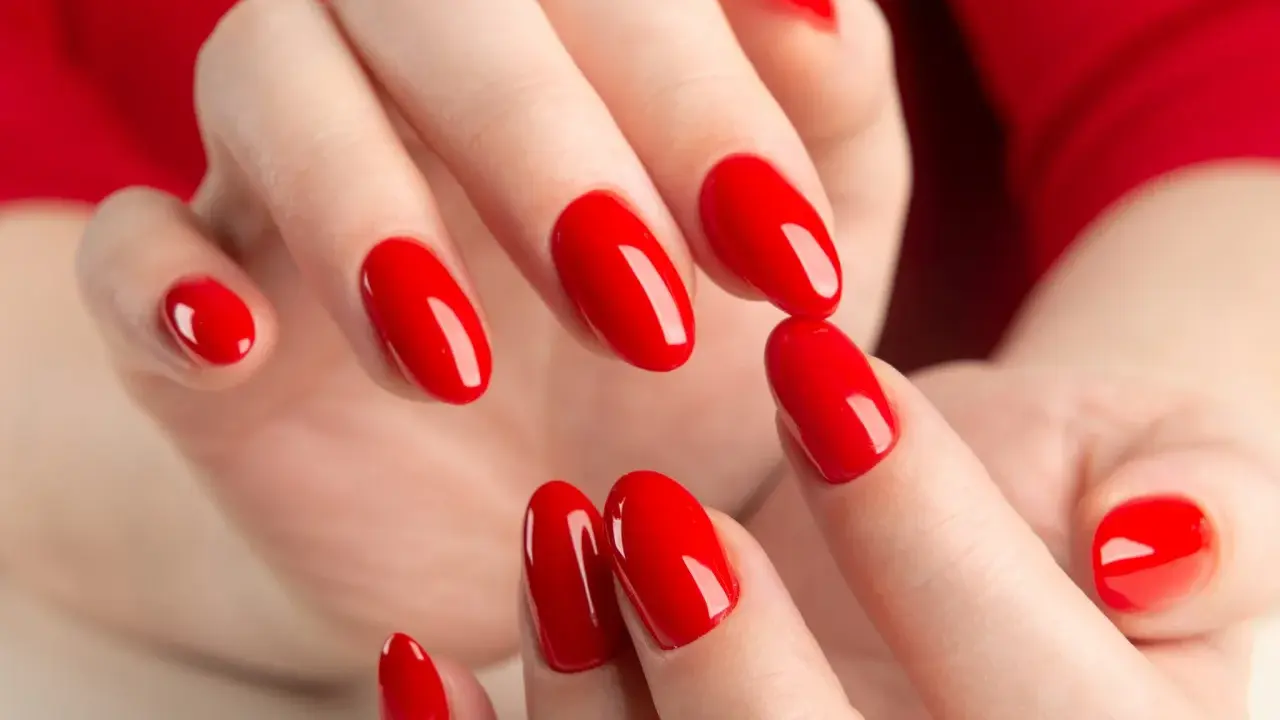 Hände mit leuchtend roten Nägeln, die die "red nail theory" verkörpern. Die glänzende Maniküre strahlt Selbstbewusstsein aus.