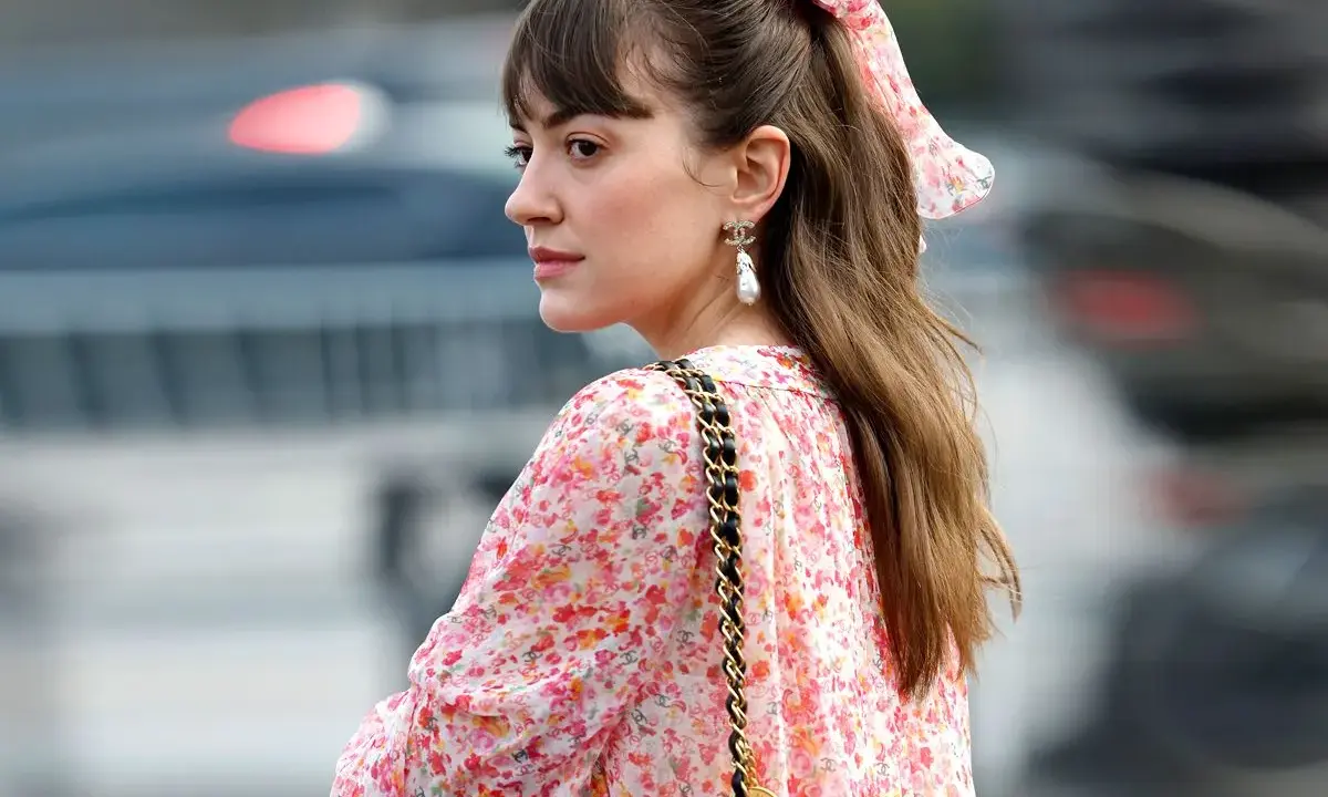 Eine Frau mit einem Blumenkleid und einer einfachen Frisur, perfekt für eine Hochzeitsgast. Ein Scrunchie mit Blumenmuster ziert ihren Pferdeschwanz.