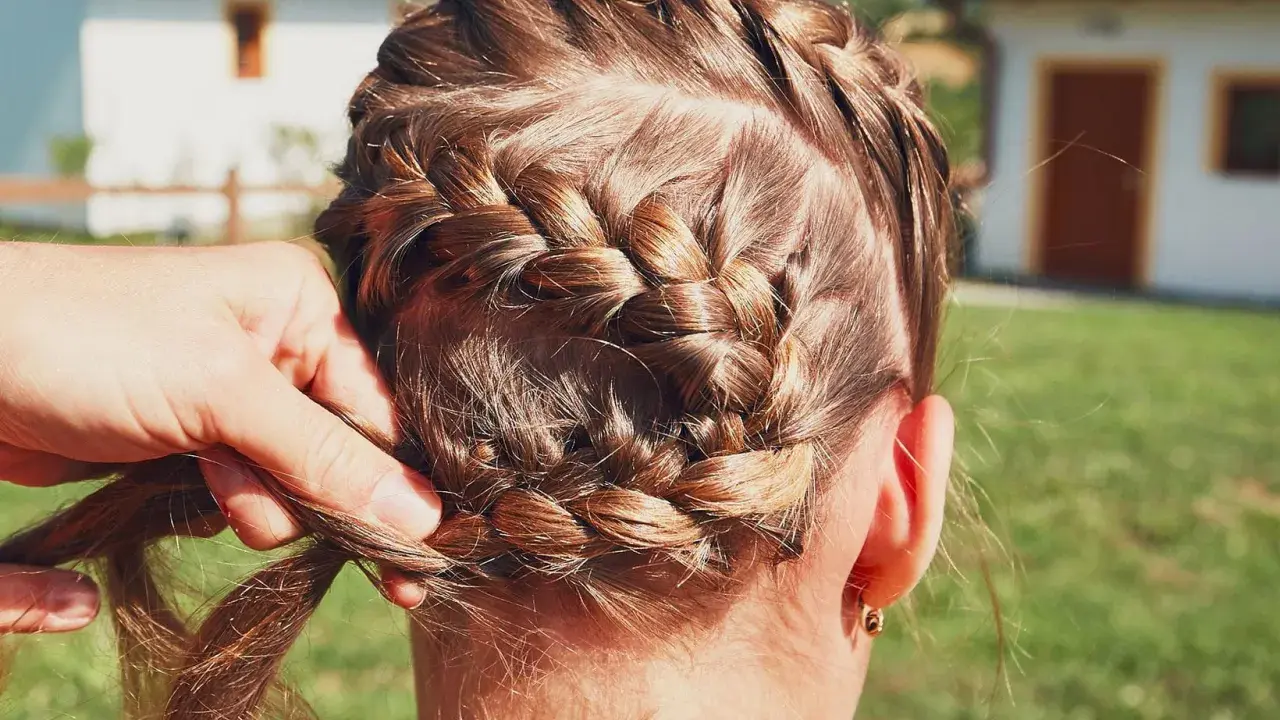 Zopf flechten für Oktoberfest Frisuren einfach. Eine Hand flechtet das braune Haar zu einem kunstvollen Zopf.