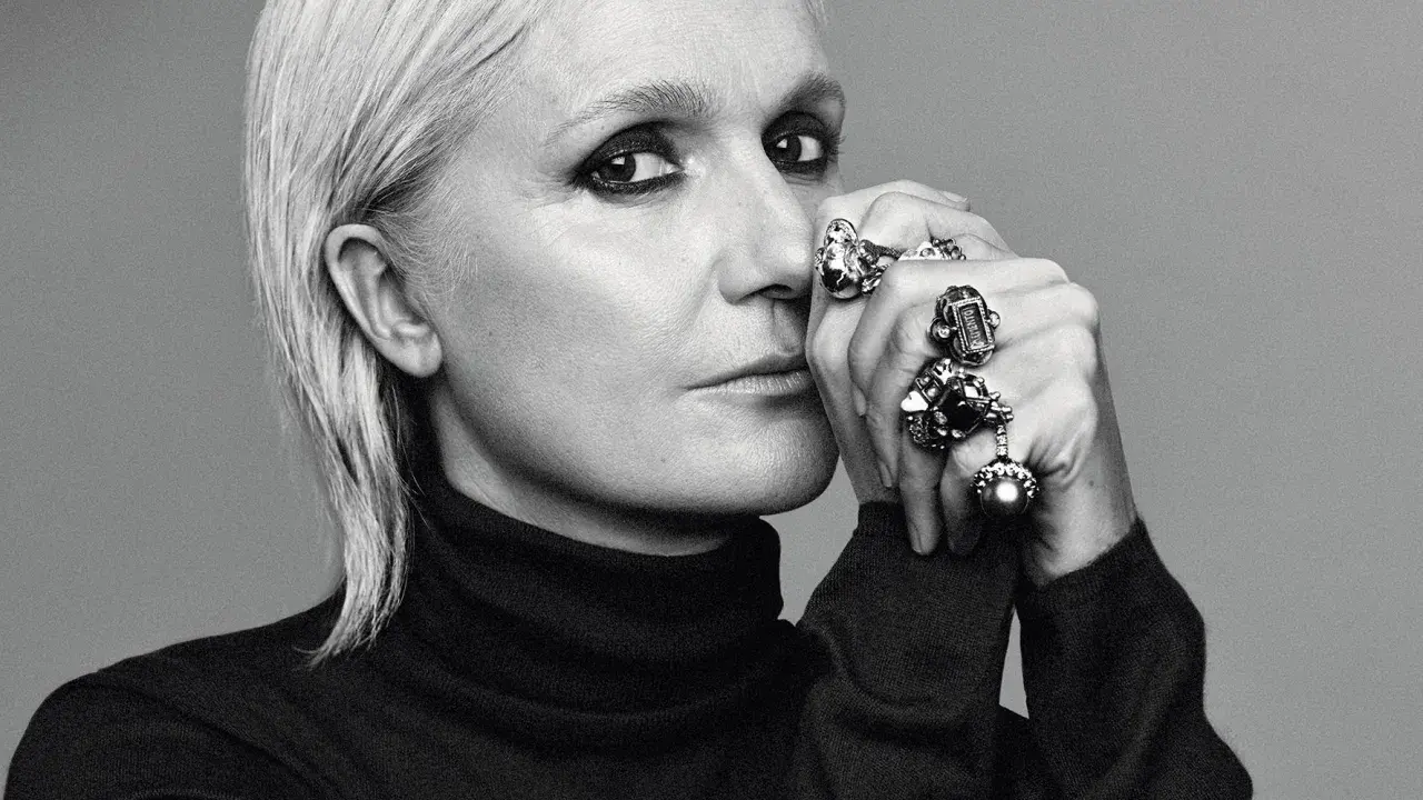 Maria Grazia Chiuri, mit markantem Make-up und vielen Ringen, blickt nachdenklich in die Kamera.