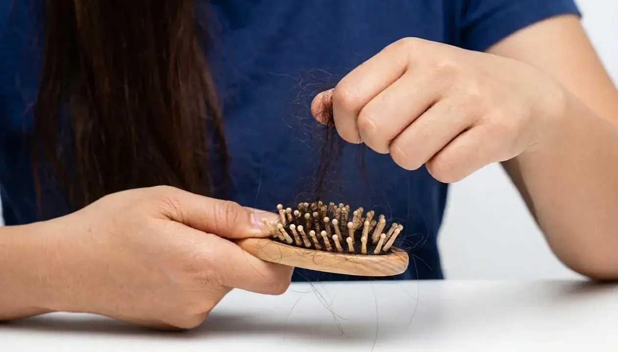 Besorgte Hände halten eine Bürste mit vielen Haaren. Was tun gegen Haarausfall? Informationen zu Ursachen und Behandlung.