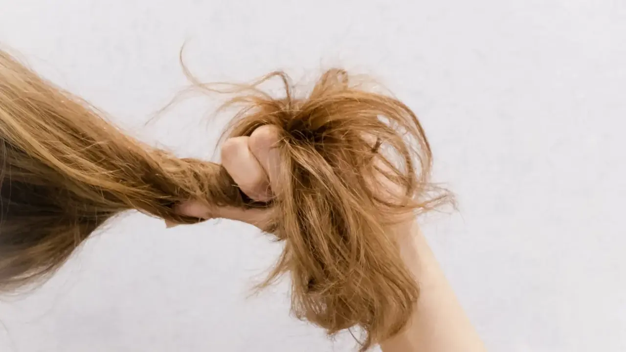 Eine Hand greift nach strohigen Haaren, die trocken und ungepflegt aussehen.