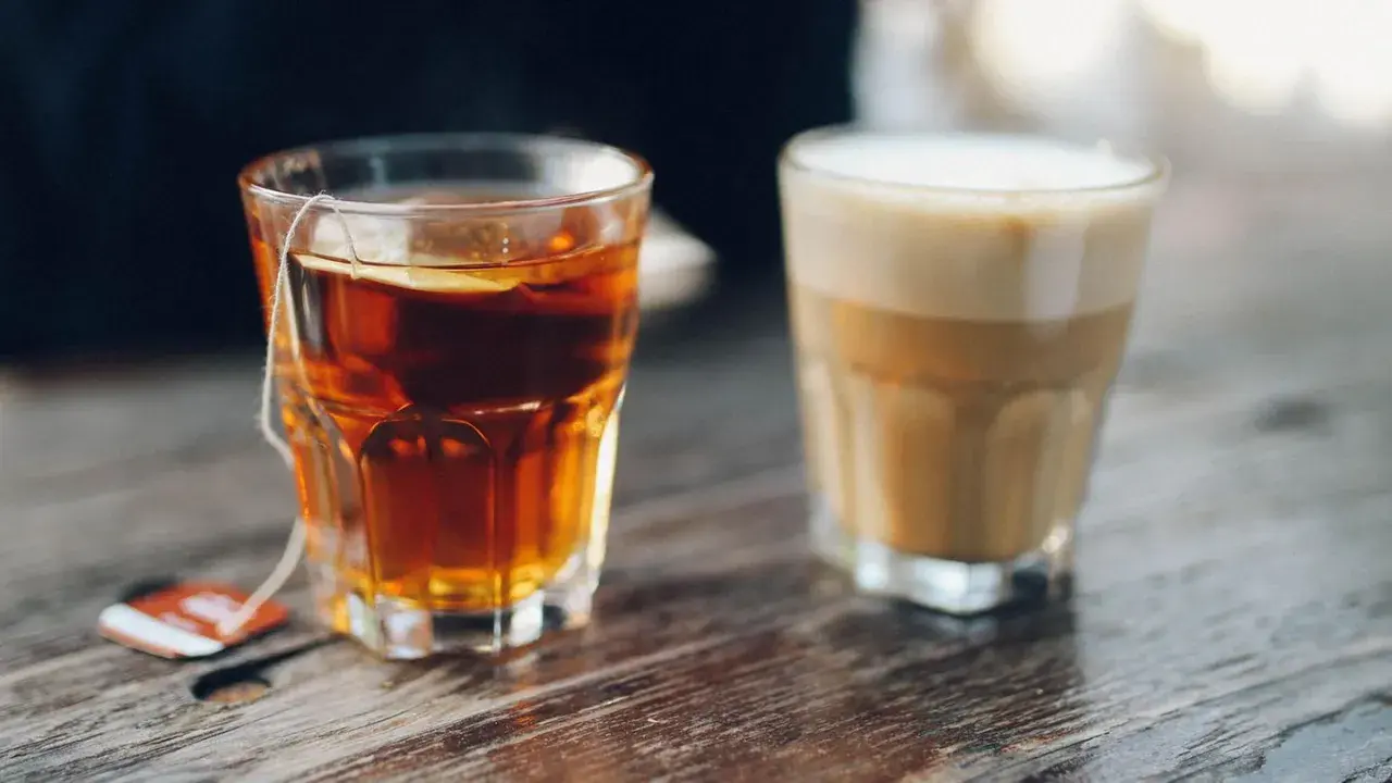 Ein Glas Tee mit Beutel und ein Latte Macchiato stehen nebeneinander. Eine leckere alternative zu Kaffee.