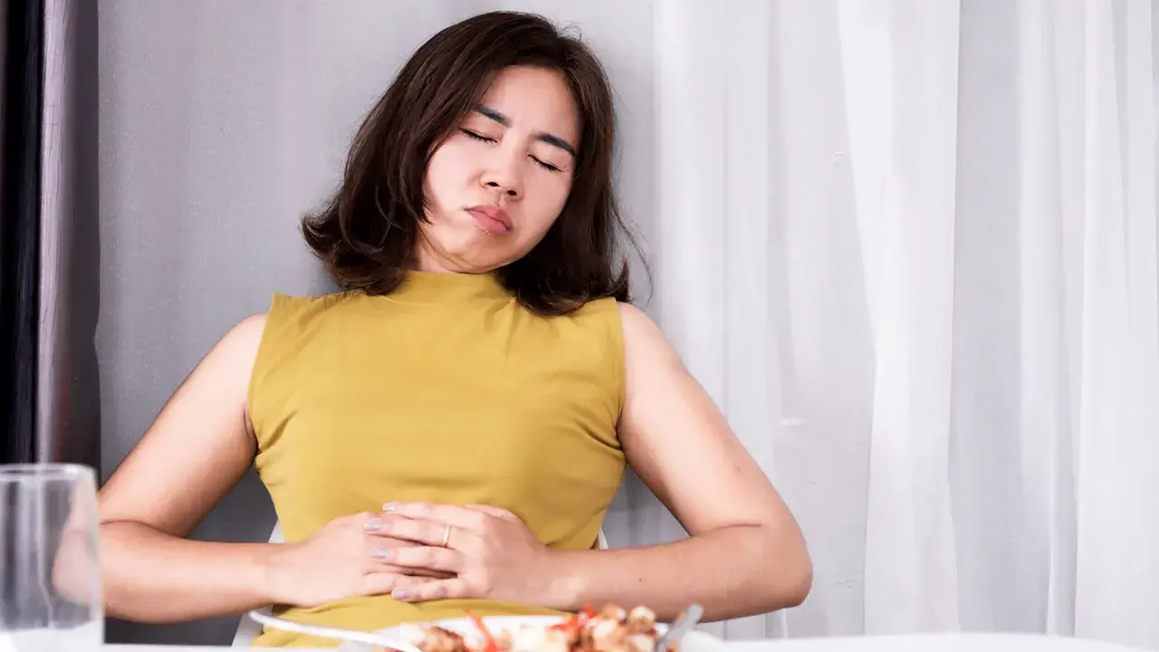 Frau mit schmerzverzerrtem Gesicht hält sich den Bauch. Sie leidet unter Bittertropfen vor oder nach dem Essen.