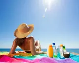 Frau mit Hut liegt am Strand, umgeben von Sonnencremes und Kokosnuss. So wird man schnell braun.