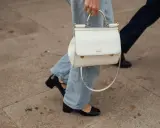 Eine Frau kombiniert lässig wide leg jeans mit schwarzen Lackschuhen und einer weißen Handtasche.