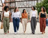 Fünf Frauen spazieren fröhlich über einen Platz. Sie zeigen, wie man Leinenhose kombinieren kann, in verschiedenen Farben und Styles.