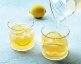 Erfrischendes zitronenwasser morgens wird in Gläser mit Eis und Zitronenscheiben gegossen.