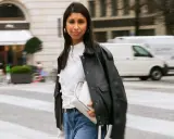 Stylische Frau kombiniert eine weiße Bluse mit Jeans und Lederjacke. Sie trägt eine weiße Tasche und goldene Ohrringe.