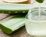 Frische Aloe Vera Blätter und ein Glas mit klarem Saft, der gerade aus einem Blatt getropft wird. Perfekt, um aloe vera saft selber machen.