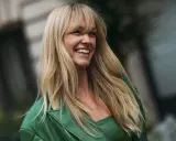 Lachende Frau mit blonden, langen Haaren und einem leichten Pony, trägt ein grünes Outfit.