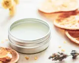 Ein Döschen mit selbstgemachtem Lippenbalsam, umgeben von getrockneten Orangen, Lavendel und Kräutern.