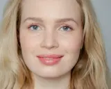 Blonde Frau mit blauen Augen und rosafarbenen Lippen, die frisch aussieht.