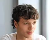 Junger Mann mit lockigem, kurzem Mullet-Haarschnitt und einem dezenten Ringohrring.