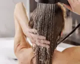 Frau wäscht sich die Haare unter der Dusche, Wasser rinnt über ihre Schultern. Eine sanfte Methode, um die Haare zu reinigen, fast wie haare waschen ohne shampoo.