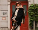 Frau mit Sonnenbrille, die einen karierten Schal lässig um den Hals gebunden hat. Sie hält eine gesteppte Tasche.