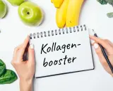 Hände halten Notizbuch mit "Kollagen-Booster". Frisches Obst und Gemüse wie Äpfel, Bananen, Sellerie, Spinat und Brokkoli liegen daneben. Eine Kollagen Lebensmittel Tabelle könnte hier inspirieren.
