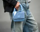 Ein hellblaues Jeans-Täschchen mit einem quadratischen Tuch binden, das den Griff ziert. Das Tuch hat ein Paisleymuster und den Schriftzug "AMIRI".