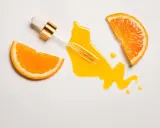 Ein Pipettenfläschchen mit leuchtend gelbem Vitamin C Serum, umgeben von saftigen Orangenscheiben. Morgens oder abends für strahlende Haut.