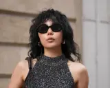 Frau mit schwarzem Wolf Cut Locken, Sonnenbrille und glitzerndem Top.