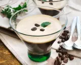 Ein Glas italienischer Eiskaffee mit Kaffeebohnen und Minze garniert, daneben Löffel und Kaffeebohnen auf einem Tuch.