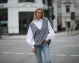 Stylische Frau in grauem Pullunder, weißer Bluse und Jeans. So lässt sich ein Pullunder kombinieren für einen lässigen Look.
