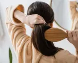 Frau kämmt ihr langes, dunkles Haar mit einer Holzbürste. Sie trägt einen flauschigen Bademantel. Tipps, wie wachsen haare schneller, sind hier nicht sichtbar.