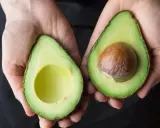 Hände halten zwei Avocadehälften. Eine Avocado mit Kern, die andere leer. Manche sagen, Avocado sei krebserregend, aber das stimmt nicht.