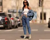 Stylisches Outfit: Eine Frau kombiniert barrel jeans mit einem weißen Top und Jeansjacke. Schlangenleder-Stiefel runden den Look ab.