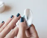Eine Hand mit dunkelblauem Nagellack wird mit einem Wattepad abgewischt, um den Nagellack zu entfernen.