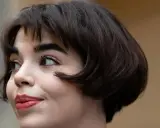 Eine Frau mit einem eleganten, dunklen short bob und rotem Lippenstift blickt nach links.