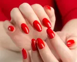 Hände mit leuchtend roten Nägeln, die die "red nail theory" verkörpern. Die glänzende Maniküre strahlt Selbstbewusstsein aus.