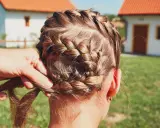 Zopf flechten für Oktoberfest Frisuren einfach. Eine Hand flechtet das braune Haar zu einem kunstvollen Zopf.