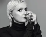 Maria Grazia Chiuri, mit markantem Make-up und vielen Ringen, blickt nachdenklich in die Kamera.