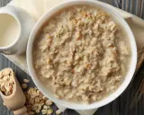 Schüssel mit Haferflocken, daneben ein Milchkännchen, Holzschaufel mit Haferflocken und Ähren. Die Haferflocken Inhaltsstoffe sind hier gut sichtbar.