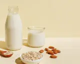 Flasche und Glas mit milchigem Getränk, daneben Mandeln und Haferflocken. Ob Mandelmilch oder Hafermilch, die Wahl ist leicht.